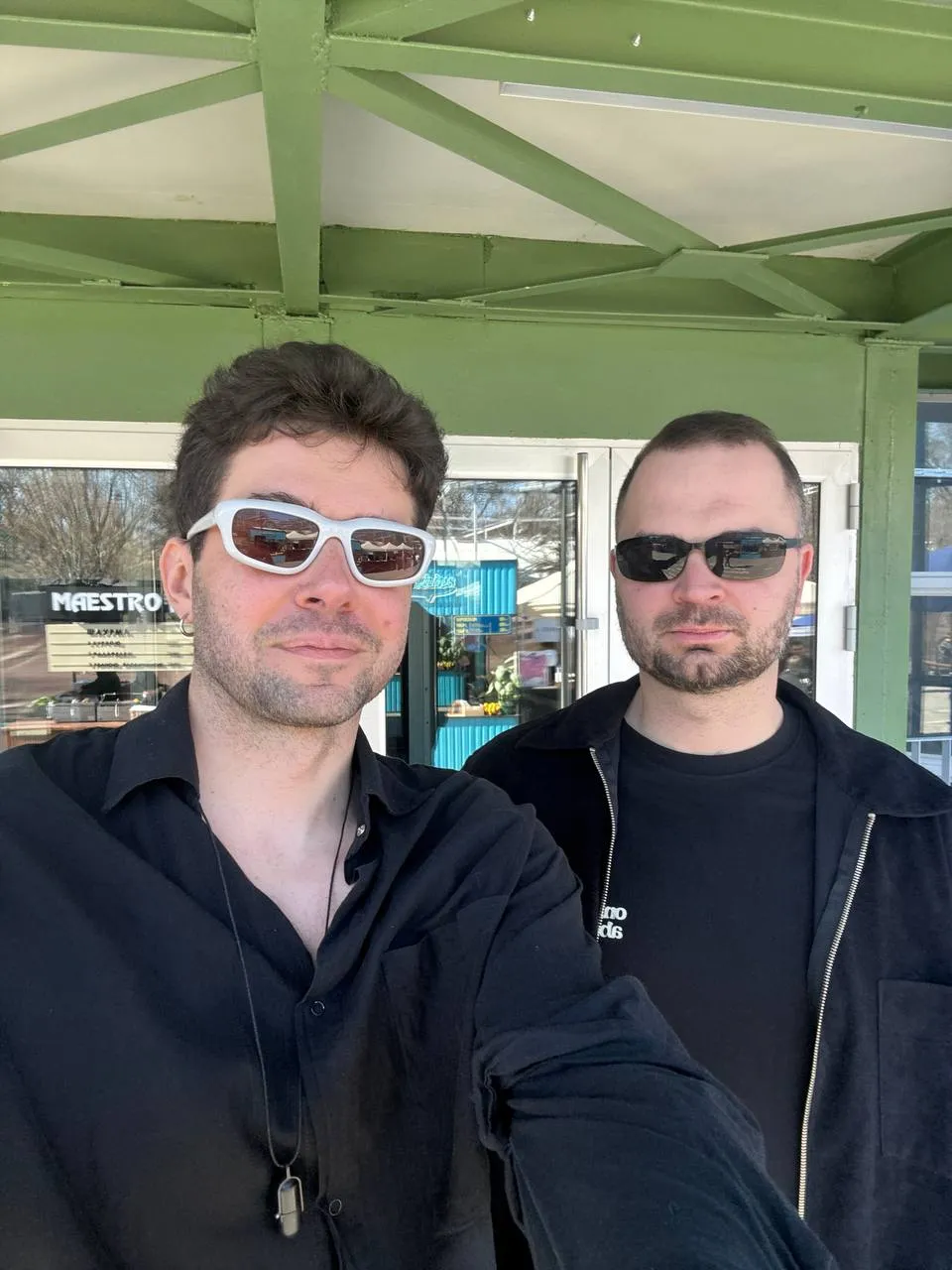 Tusella founders Artem and Mykyta side by side in sunglasses under the green roof of a market pavilion